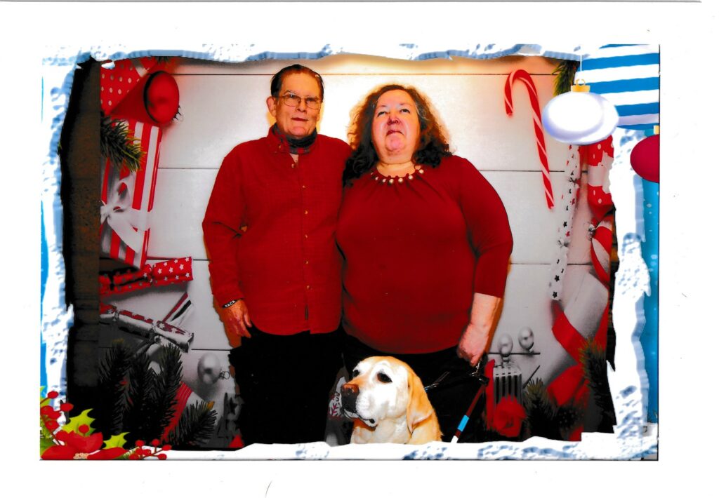 Annieand  Jerry smiling at the camera standing in matching holiday colors and Bailey the yellow lab at their feet.