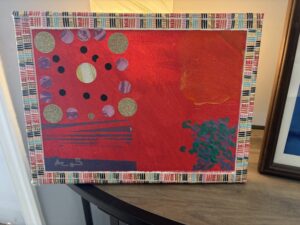 12 x 7 horizontal canvas painting.
The painting's background is primarily a vivid red with
textured brush strokes and is sectioned in
four uneven quadrants.
On the upper left quadrant of the painting,
there is a series of circular shapes
arranged in a rough square pattern.
These circles include larger gold glittery circles, medium-sized lavender circles
with a marbled texture
, and smaller solid black circles
. Inside this pattern of circles,
near its center, is an off-white circle
with faint greenish lines suggesting a planet-like shape.
In the lower left quadrant
there are horizontal, brush-stroked lines in purple and blue hues.
On the right side of the painting,
there is an irregular orange shape in the upper right quadrant and a shimmery green abstract shape
on the bottom left quadrant.
The painting is bordered by geometric-patterned washy tape
with small rectangular blocks of colors including white, blue, and red.
