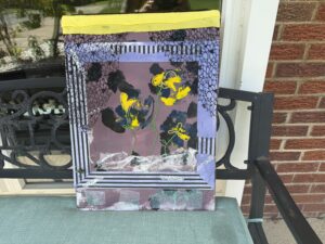 wall art resembling a window with black net curtains parted revealing an inner window looking out on three flowers. Colors are purple, gray, yellow and black. A beded resembling a bug sits in the bottom left corner .